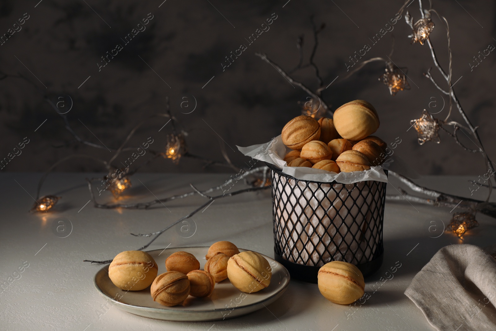 Photo of Aromatic walnut shaped cookies and decorative branch with lights on white table. Homemade pastry carrying festive atmosphere