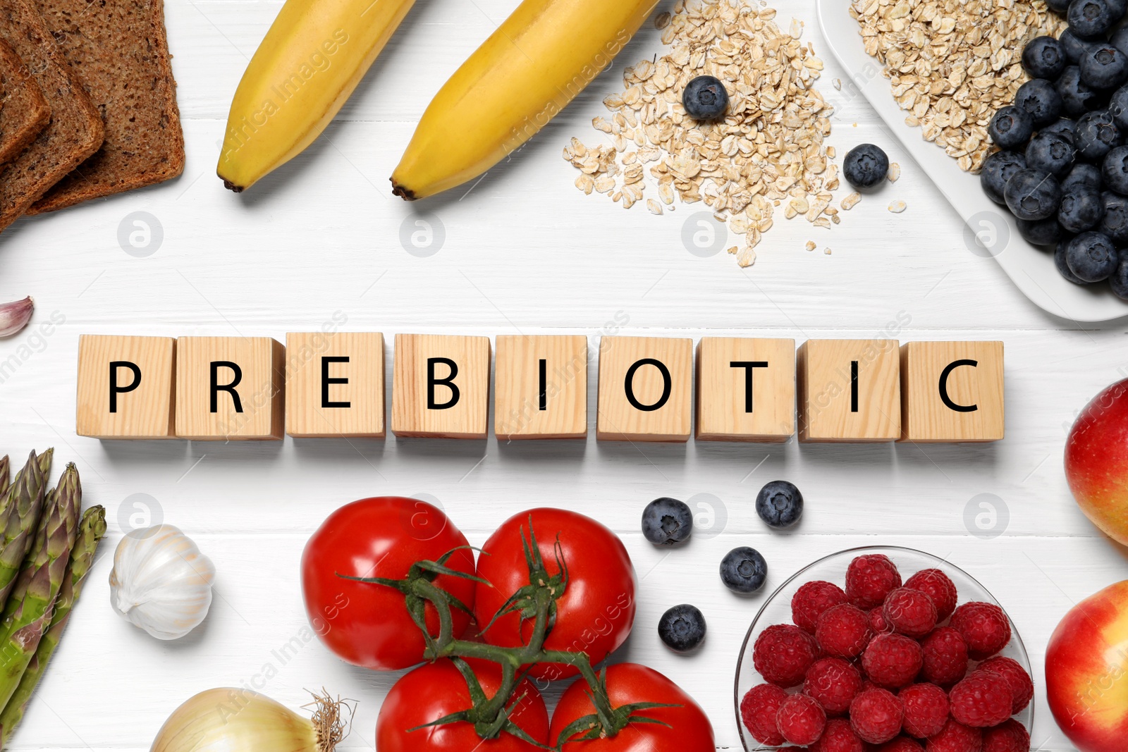 Photo of Word Prebiotic made of cubes with letters and foodstuff on white wooden table, flat lay