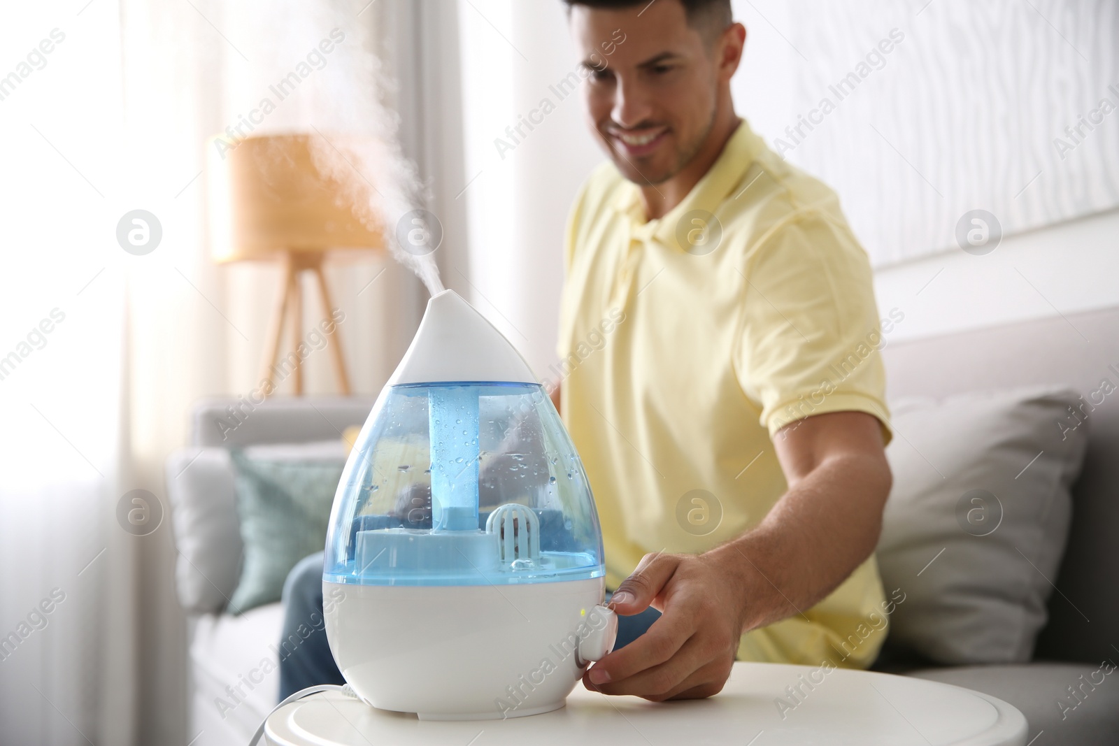 Photo of Man using modern air humidifier at home, focus on hand