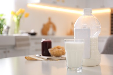 Photo of Gallon bottle of milk, glass and breakfast cereal on white table in kitchen. Space for text