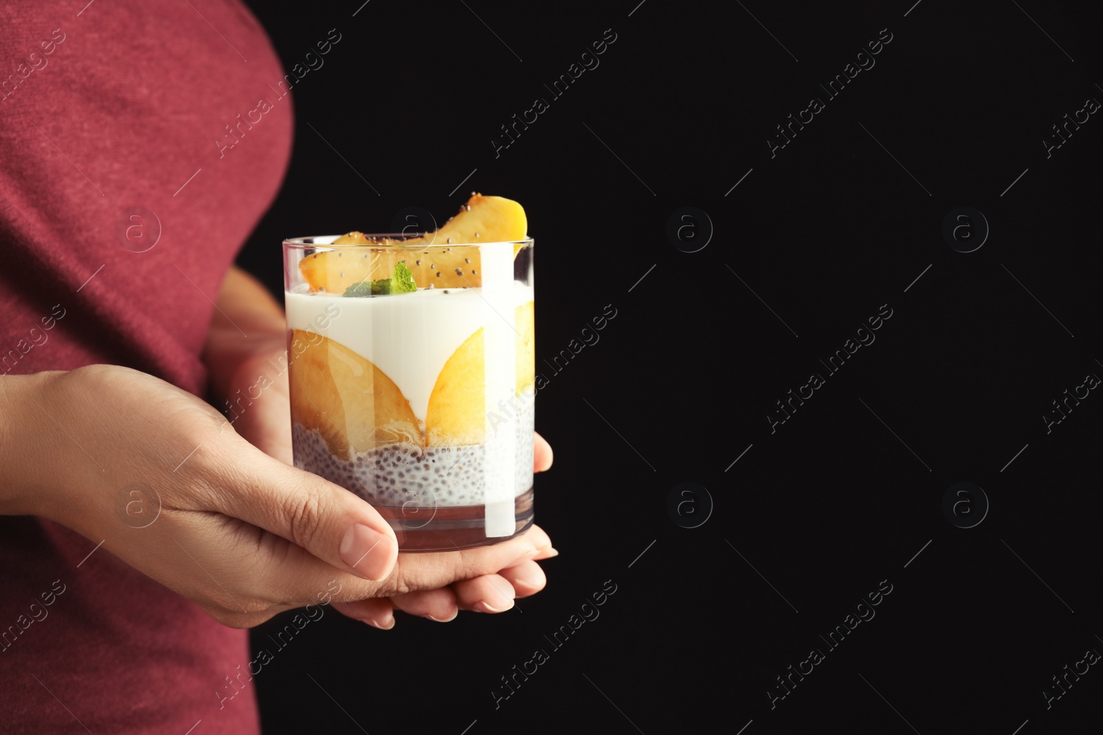 Photo of Woman holding tasty peach dessert with yogurt and chia seeds on black background, closeup. Space for text