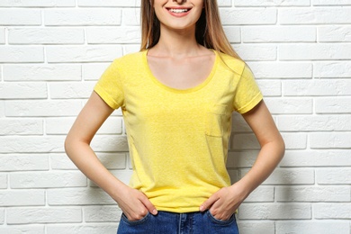 Young woman wearing blank t-shirt near white brick wall, closeup. Mockup for design