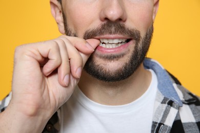 Photo of Man biting his nails on yellow background, closeup