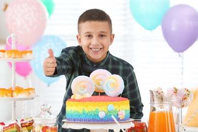 Photo of Happy boy at table with treats in room decorated for birthday party