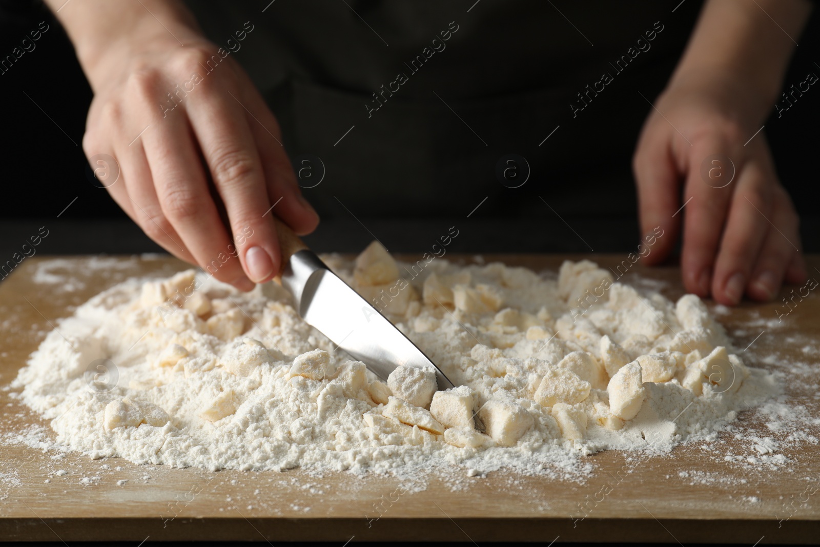 Photo of Woman making shortcrust pastry with knife at table, closeup