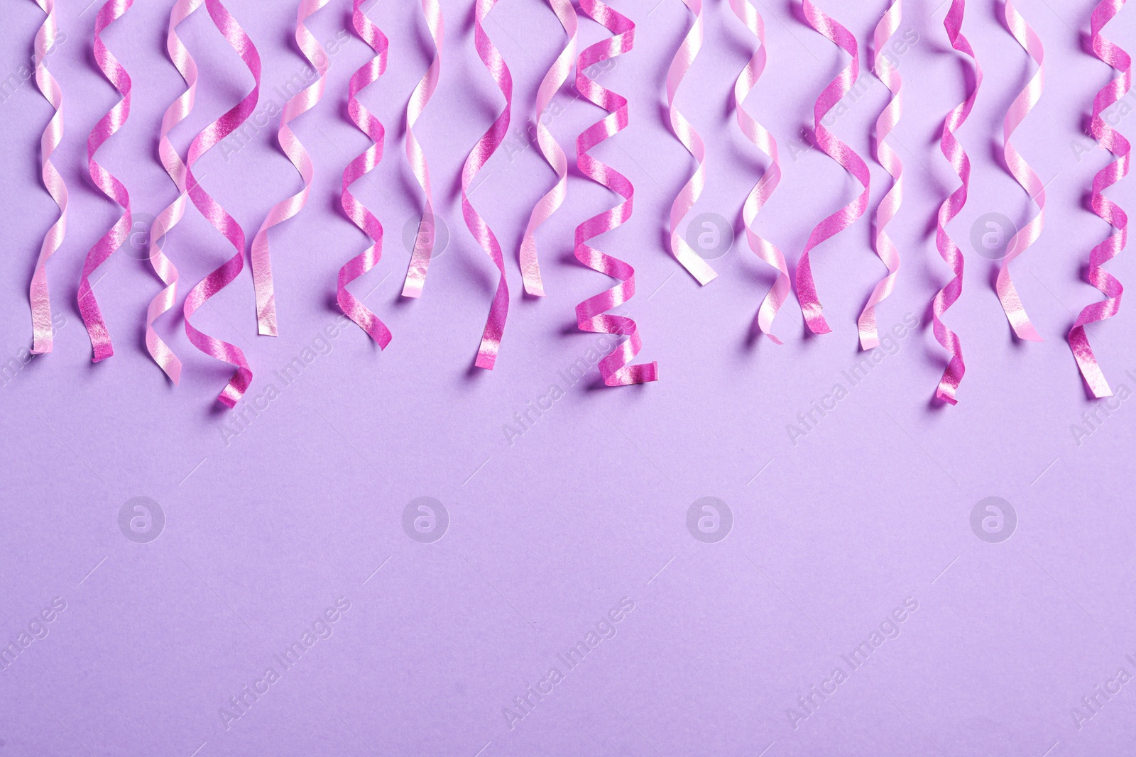 Photo of Pink serpentine streamers on light violet background, flat lay. Space for text