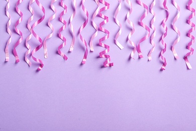 Photo of Pink serpentine streamers on light violet background, flat lay. Space for text