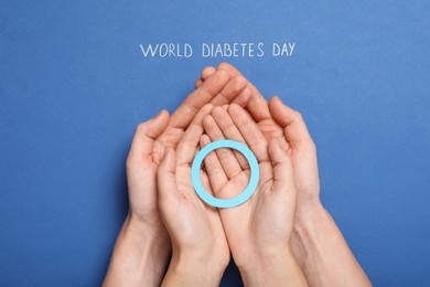 Photo of People holding blue paper circle near text World Diabetes Day on color background, top view