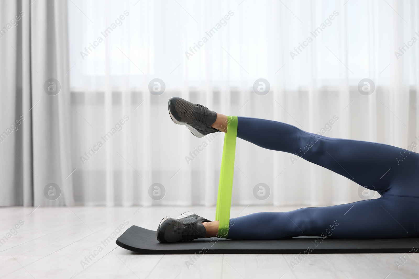 Photo of Woman doing exercise with fitness elastic band on mat indoors, closeup