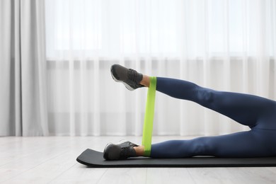 Woman doing exercise with fitness elastic band on mat indoors, closeup