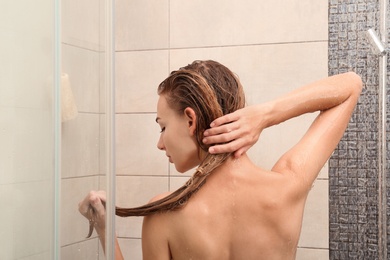 Photo of Young woman washing hair in shower at home