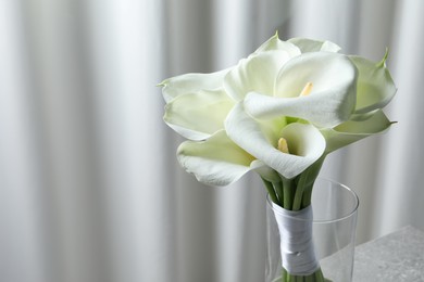 Beautiful calla lily flowers in glass vase, closeup. Space for text