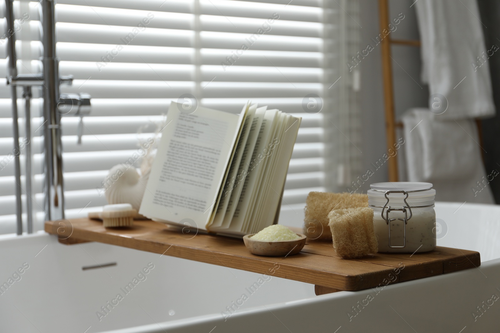 Photo of Wooden tray with spa products and book on bath tub in bathroom