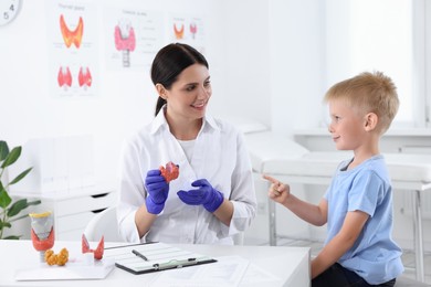 Photo of Endocrinologist showing thyroid gland model to little patient at table in hospital