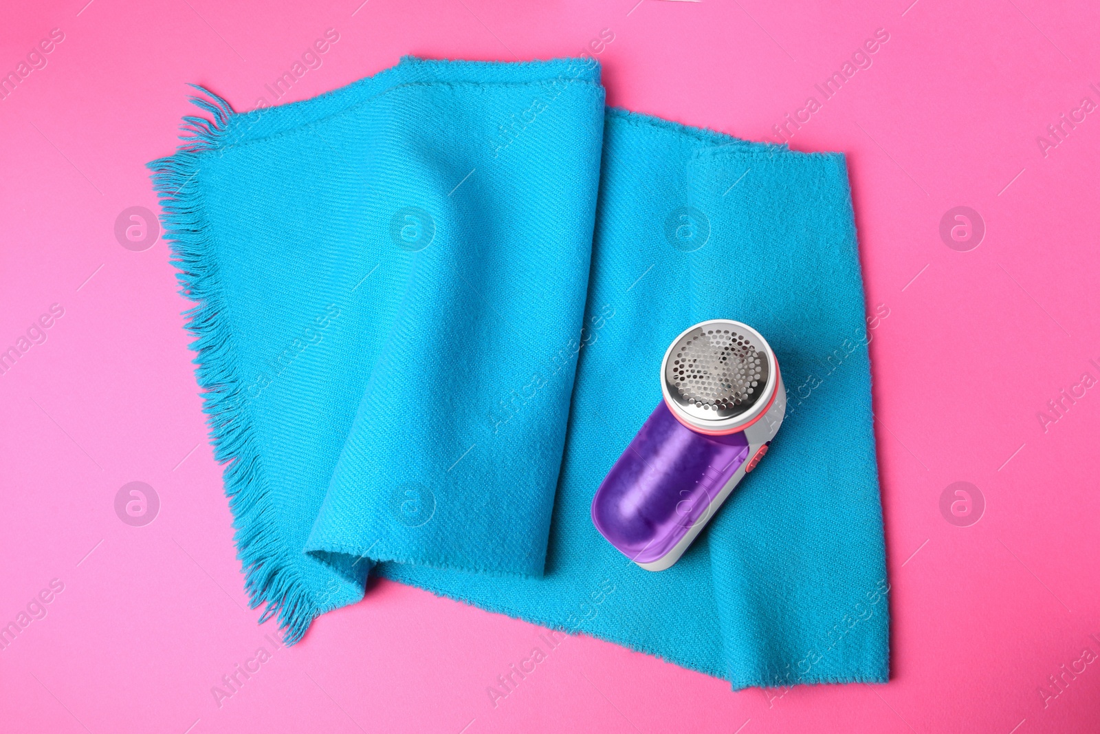 Photo of Light blue scarf and fabric shaver on pink background, top view