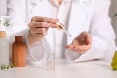 Photo of Dermatologist testing essential oil at white table, selective focus