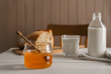 Photo of Jar with honey, milk and bread on white wooden table