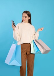Photo of Happy young woman with shopping bags and smartphone on light blue background. Big sale