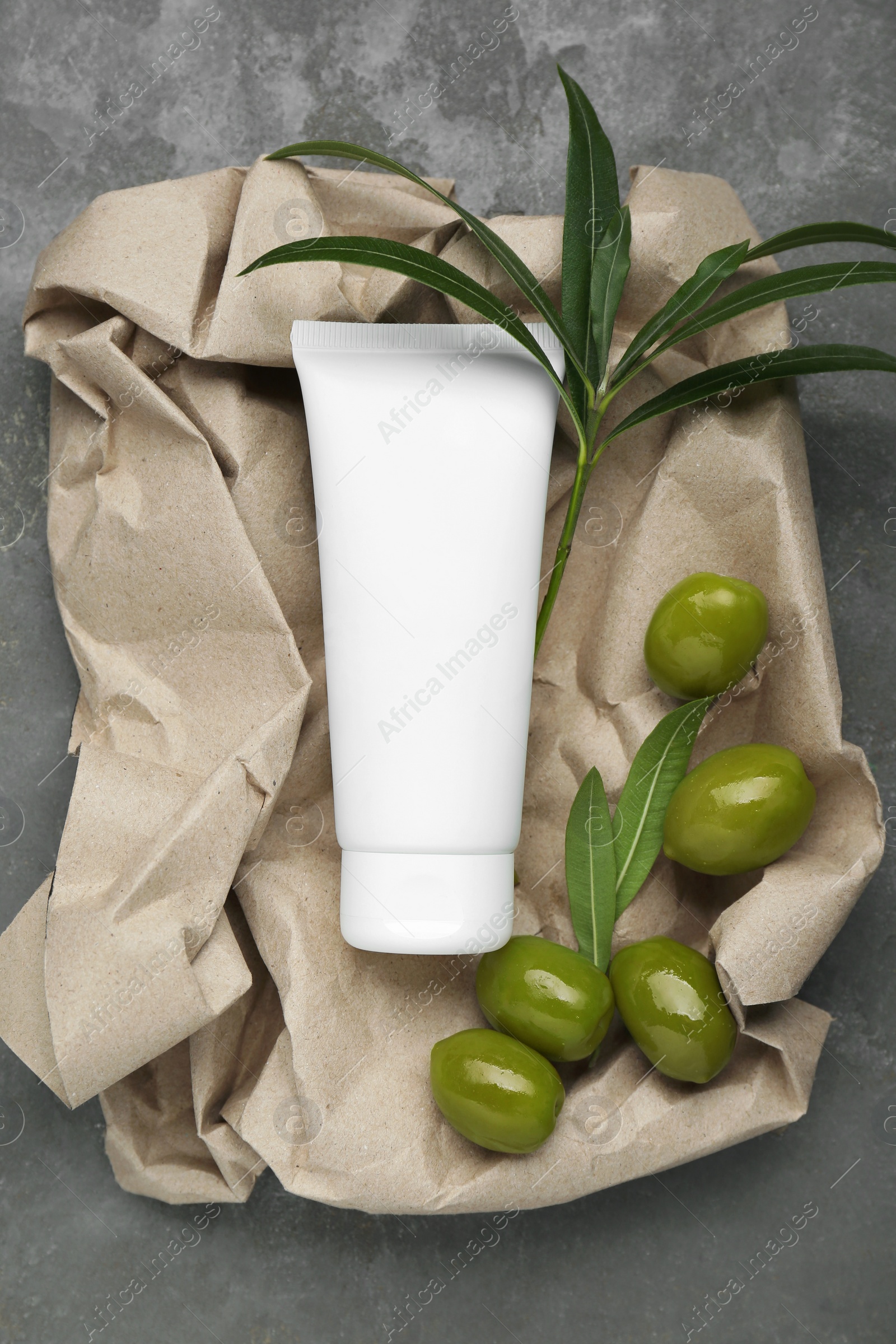 Photo of Tube of cream with olive essential oil and kraft crumpled paper on dark grey table, top view