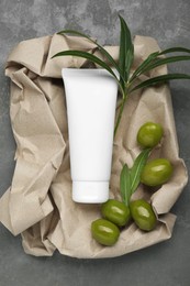 Photo of Tube of cream with olive essential oil and kraft crumpled paper on dark grey table, top view