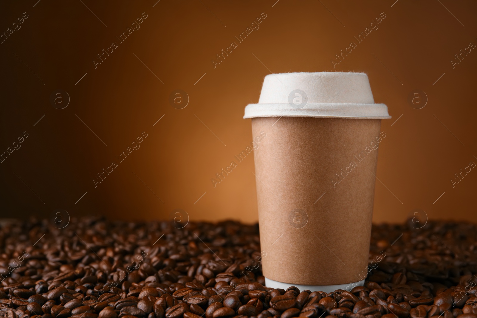 Photo of Coffee to go. Paper cup on roasted beans against brown background, space for text