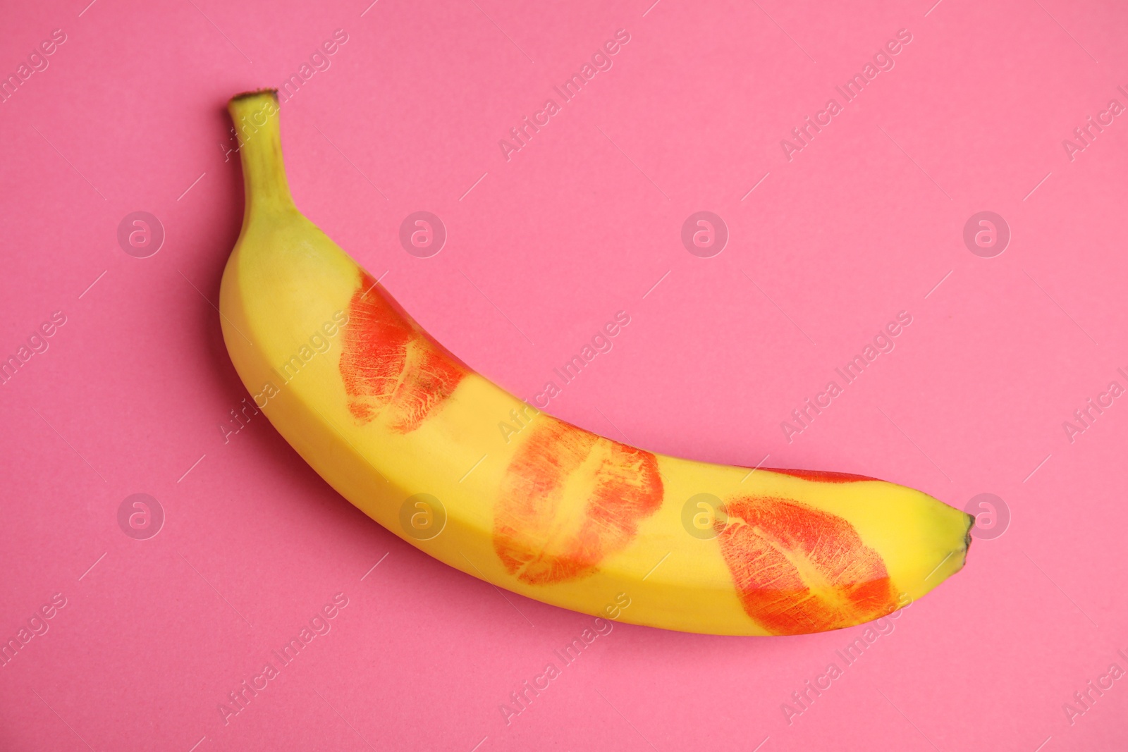 Photo of Top view of fresh banana with red lipstick marks on pink background. Oral sex concept