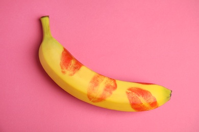 Top view of fresh banana with red lipstick marks on pink background. Oral sex concept