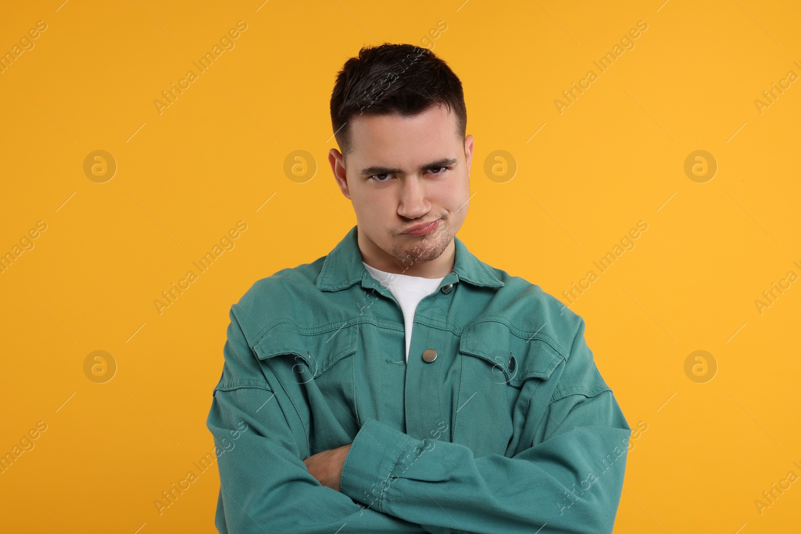 Photo of Portrait of resentful man with crossed arms on orange background