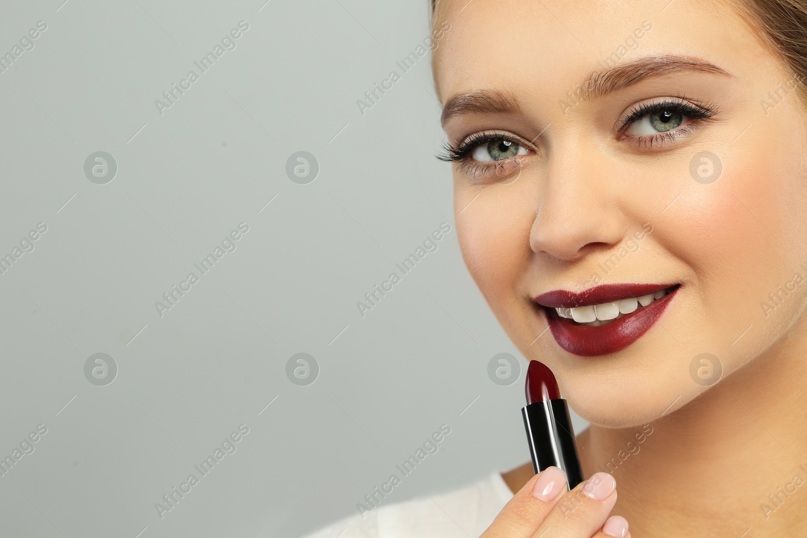 Photo of Beautiful woman applying dark lipstick on gray background. Space for text