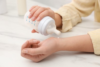 Photo of Woman checking infant formula temperature at white table, closeup. Baby milk