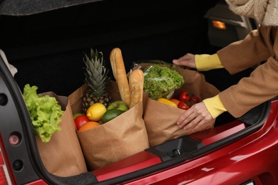 Photo of Young woman putting bags of groceries into her car, closeup