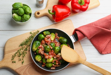 Flat lay composition of tasty roasted Brussels sprouts with bacon on white wooden table