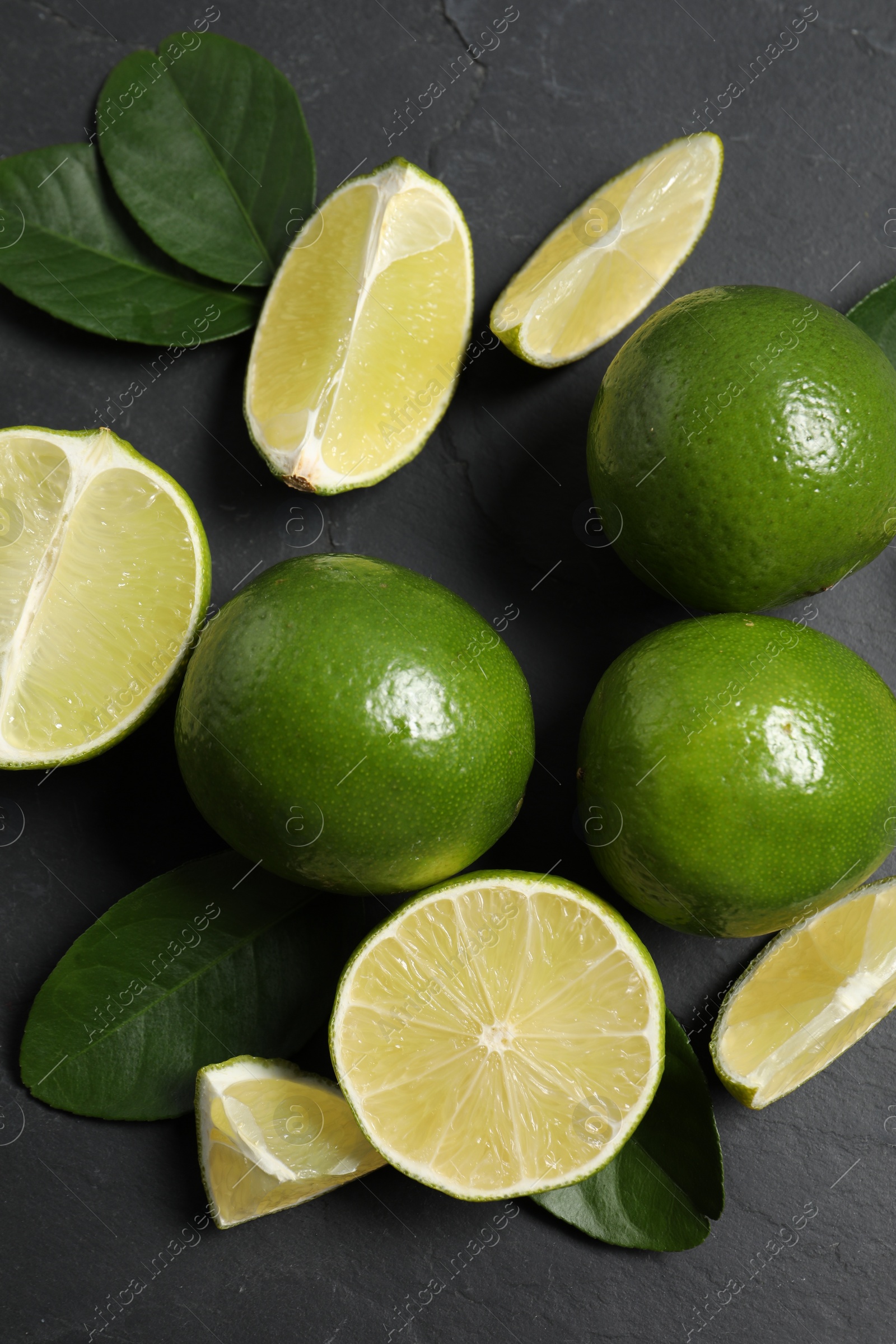 Photo of Fresh ripe limes and leaves on black table, top view