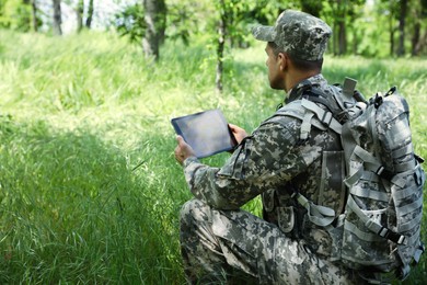 Photo of Soldier with backpack using tablet in forest