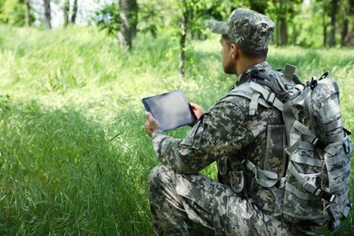 Soldier with backpack using tablet in forest