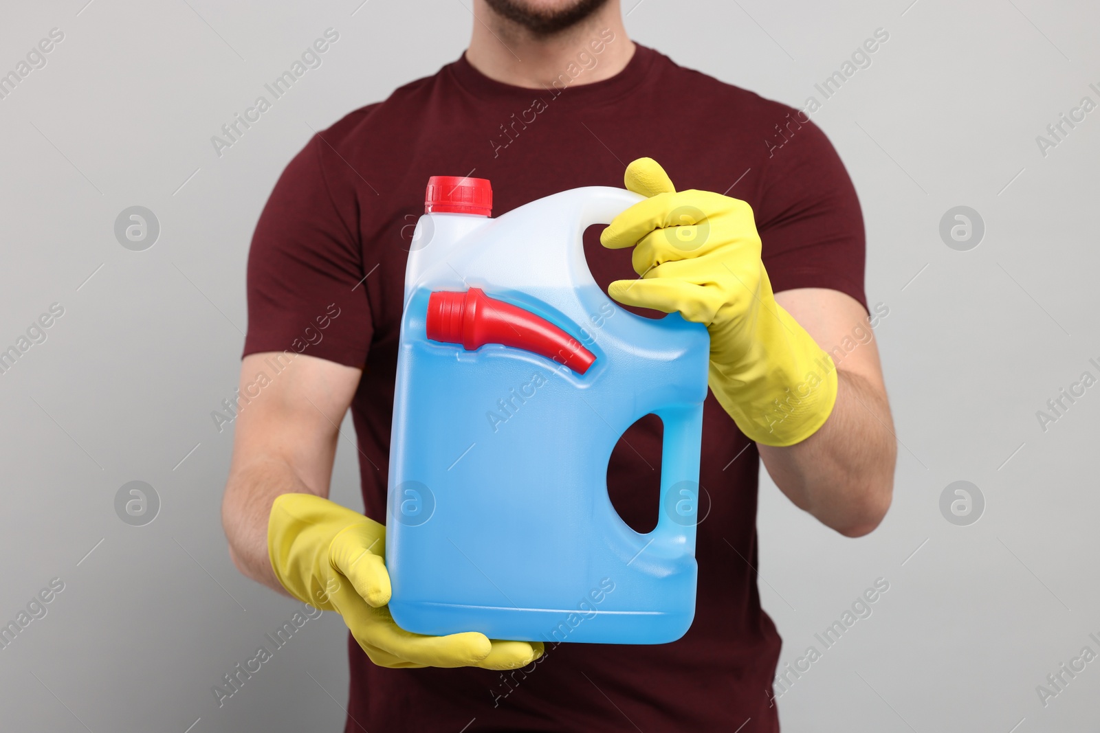 Photo of Man holding canister with blue liquid on light grey background, closeup