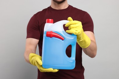 Man holding canister with blue liquid on light grey background, closeup