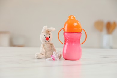 Photo of Baby bottle, toy and pacifier on white marble table indoors. Maternity leave concept