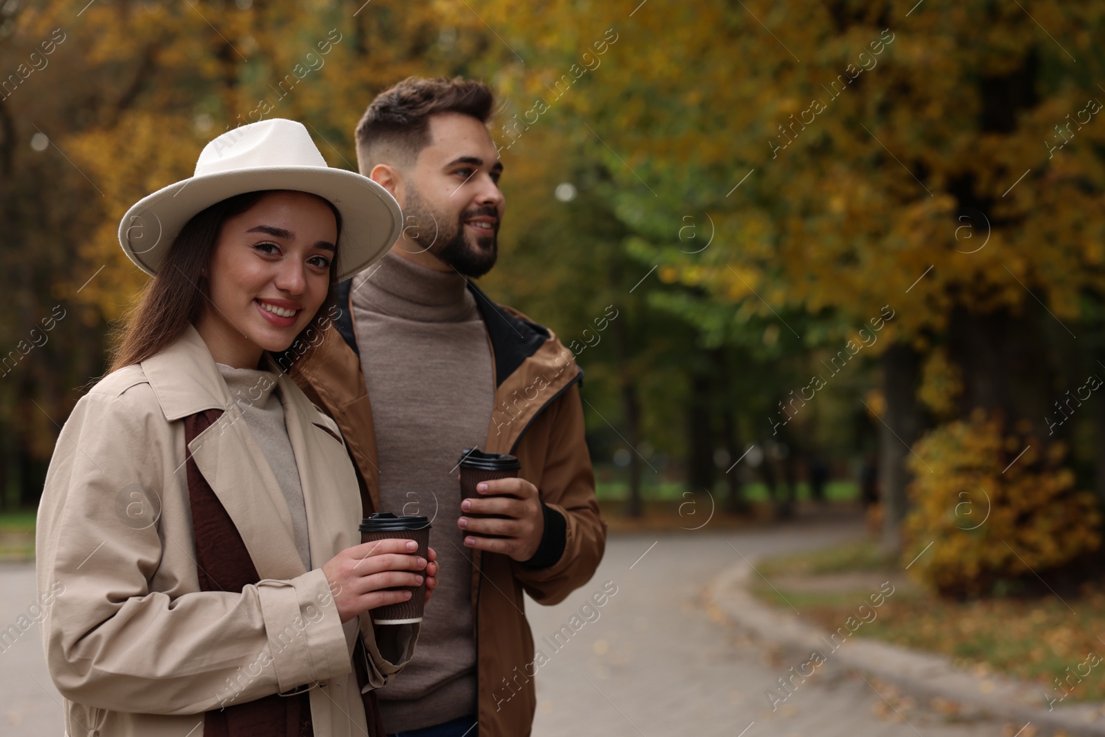 Photo of Happy young couple with cups of coffee spending time together in autumn park, space for text