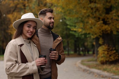 Happy young couple with cups of coffee spending time together in autumn park, space for text
