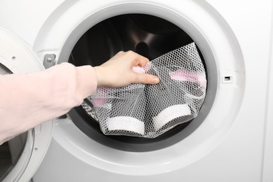 Photo of Woman putting stylish sneakers into washing machine, closeup