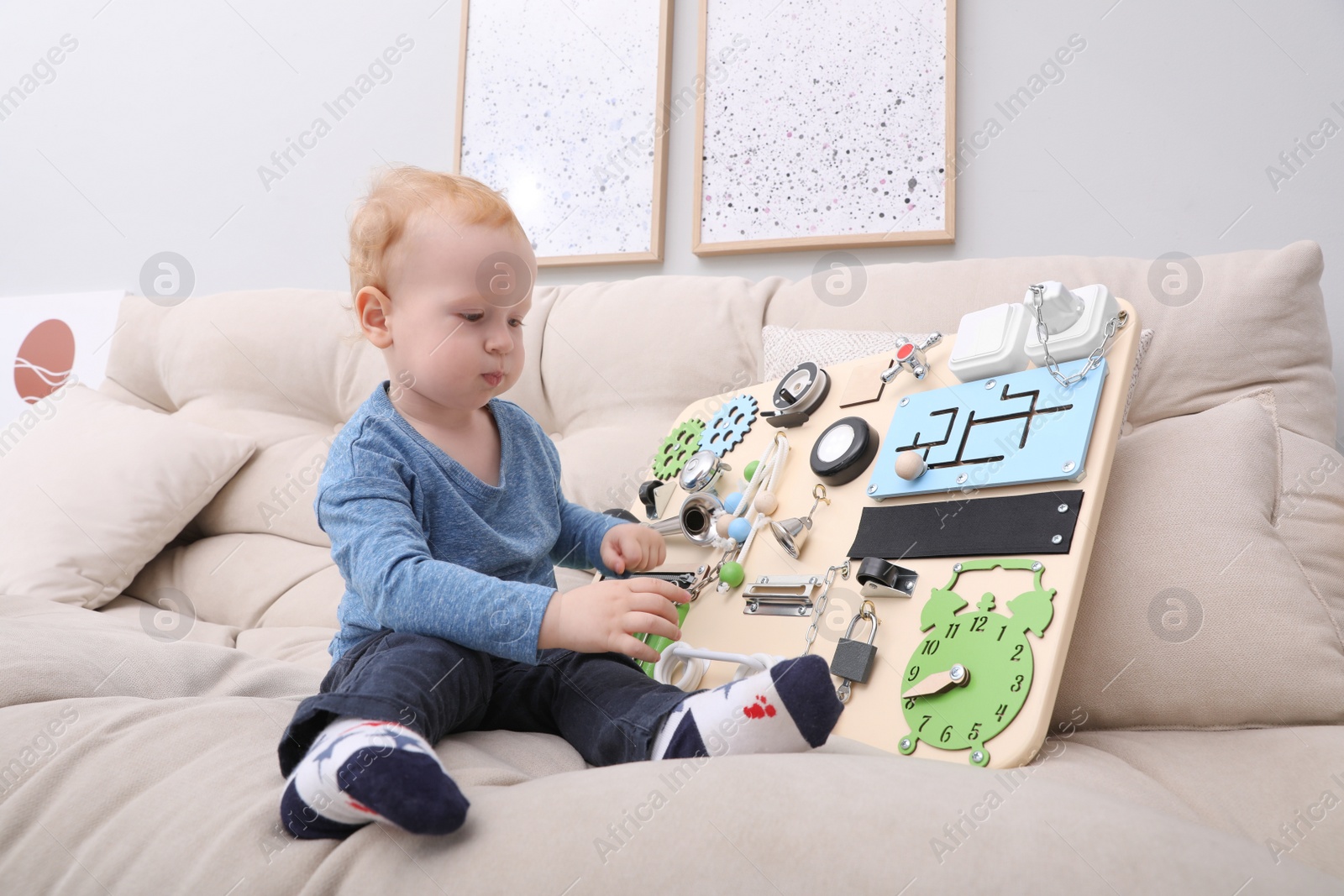 Photo of Cute little boy playing with busy board on sofa at home