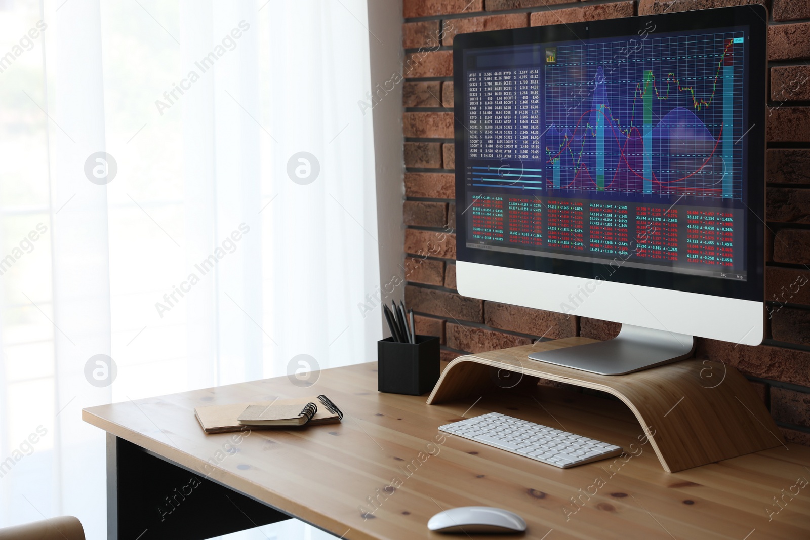 Photo of Modern computer with statistic information on wooden table near brick wall