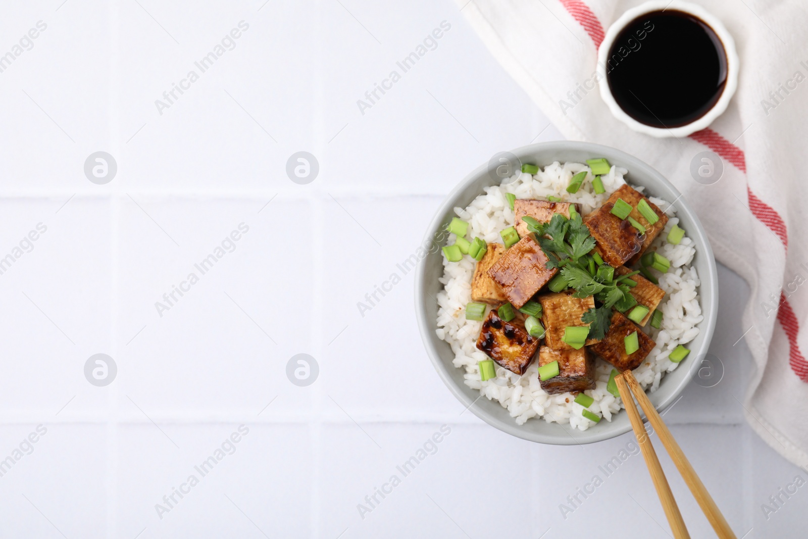 Photo of Delicious rice with fried tofu and greens served on white tiled table, flat lay. Space for text