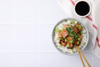 Delicious rice with fried tofu and greens served on white tiled table, flat lay. Space for text