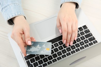 Online payment. Woman using credit card and laptop at white wooden table, top view