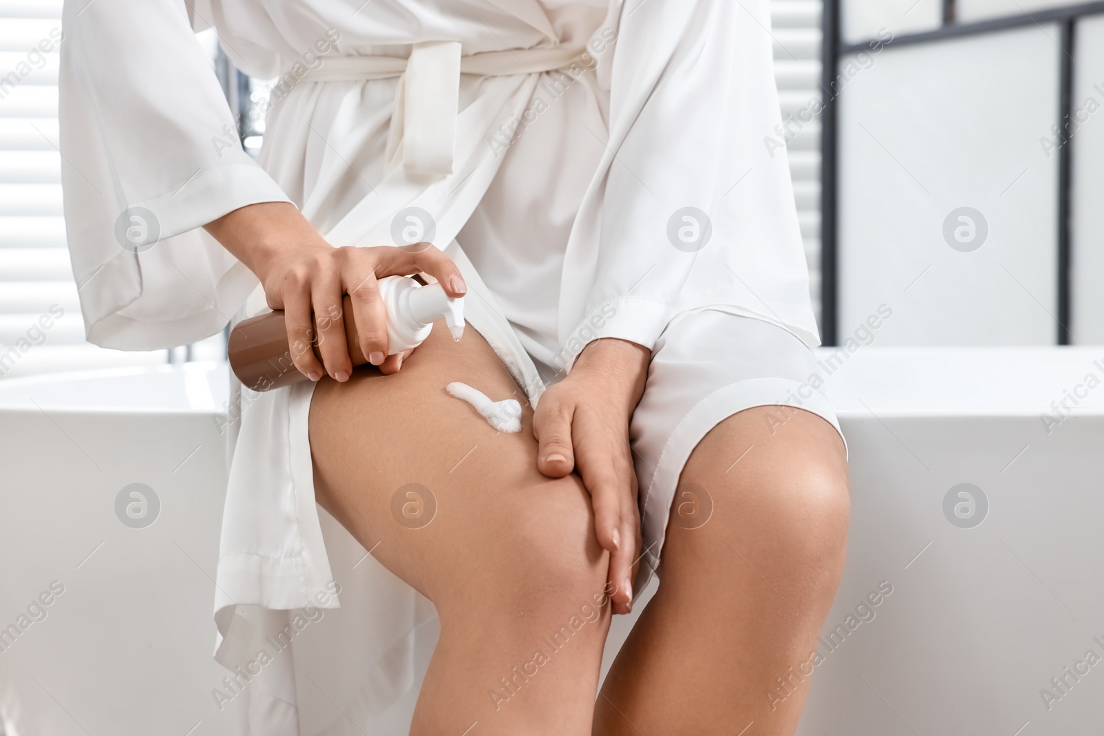 Photo of Woman applying self-tanning product onto her leg on tub in bathroom, closeup