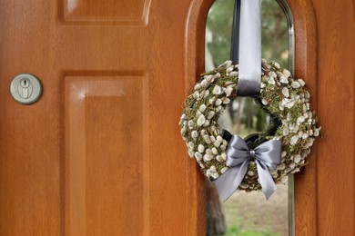 Photo of Wreath made of beautiful willow branches and grey bow on wooden door, space for text