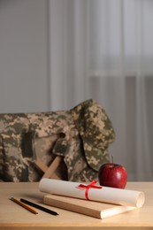 Photo of Diploma, apple and stationery on wooden table indoors. Military education