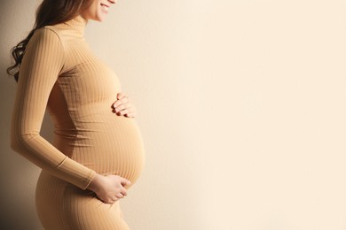 Pregnant woman touching her belly on beige background, closeup. Space for text